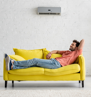 handsome smiling man lying on yellow sofa under air conditioner at home