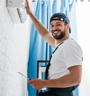 Smiling workman looking at camera while repairing air conditioner