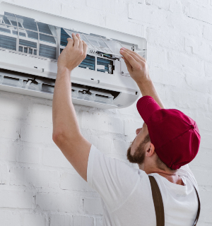 young repairman changing filter for air conditioner hanging on white brick wall